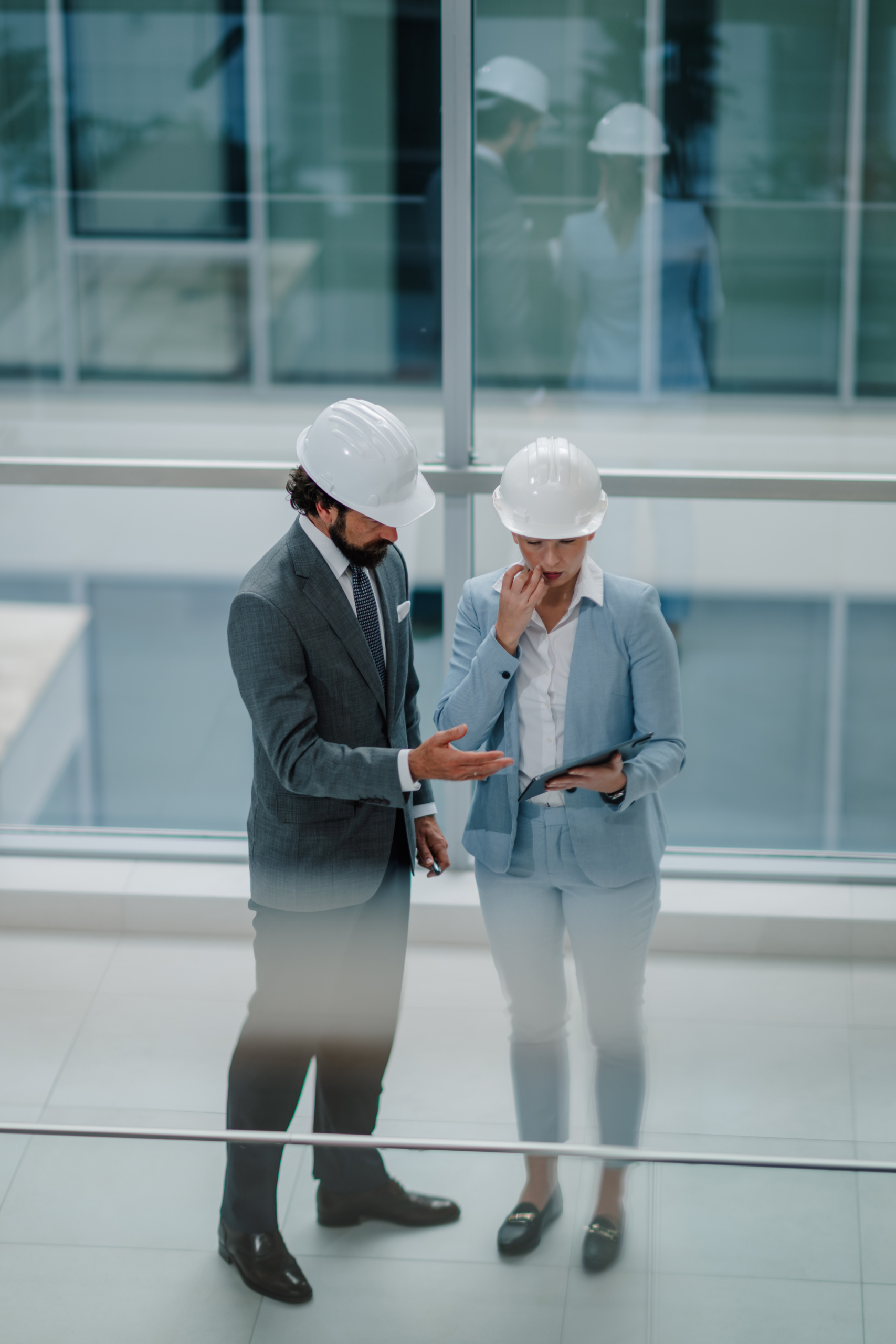 Architects discussing blueprint on tablet in modern office building Architects discussing blueprint on tablet in modern office building